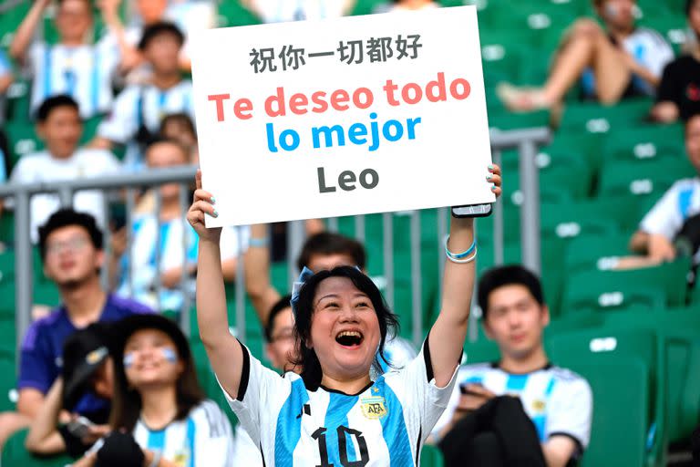 A football fan wears an Argentina football jersey showing the number of Argentinian star Lionel Messi as she holds a board saying 