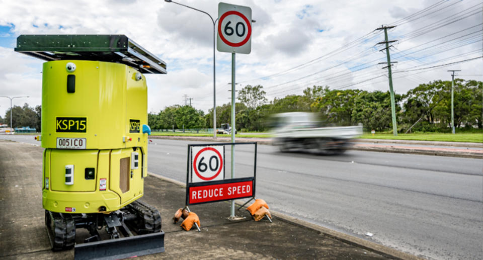 The new speed camera next to a road and speed sign.