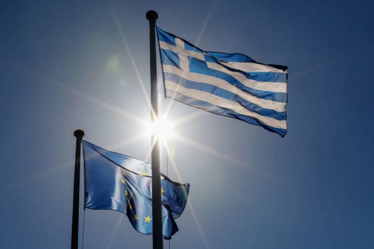 The nationa Greek flag (R) and European Union flag (EU)  flutter in the breeze as the sun shines in Athens, Greece on October 5, 2021. (Photo by David GANNON / AFP)