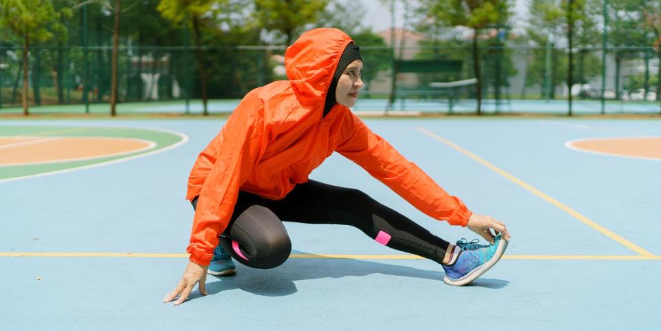 sporty muslim woman and runner with hijab stretching legs in the park