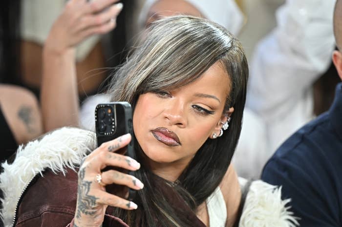 Rihanna takes a selfie with a serious expression. She wears a furry jacket and elaborate ear jewelry