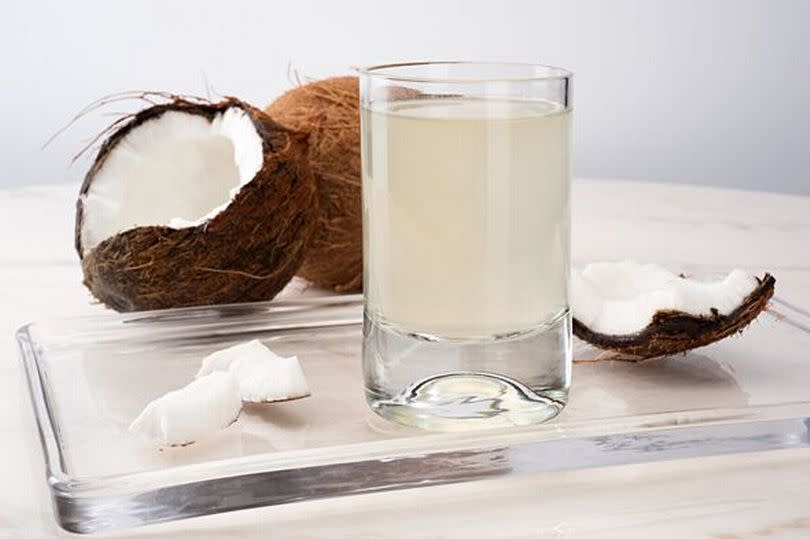 A glass of coconut water next to a slice coconut