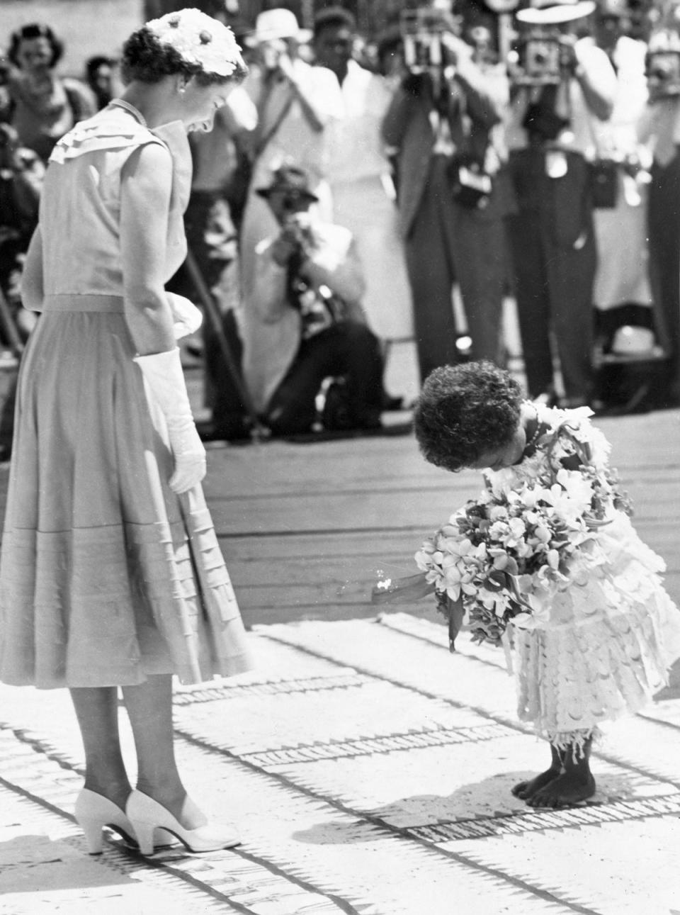 Fiji, 1953: The Queen smiles down at Mei Kainona, as the four year old Fijian girl bows gravely before presenting her with a bouquet of native flowers in Suva. (PA Archive/PA Images)