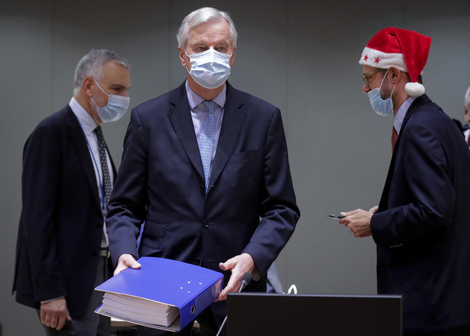 A colleague wears a Christmas hat as European Union chief negotiator Michel Barnier, center, carries a binder of the Brexit trade deal during a special meeting of Coreper, at the European Council building in Brussels, Friday, Dec. 25, 2020. European Union ambassadors convened on Christmas Day to start an assessment of the massive free-trade deal the EU struck with Britain. After the deal was announced on Thursday, EU nations already showed support for the outcome and it was expected that they would unanimously back the agreement, a prerequisite for its legal approval. (Olivier Hoslet, Pool via AP)