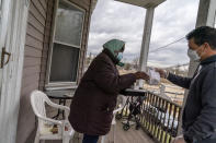 Dominga Costa, 88, left, receives a Thanksgiving dinner and some cookies from Meals on Wheels volunteer, Ted Fischer, Wednesday, Nov. 25, 2020, at her home in Providence, R.I. As more at-risk seniors find themselves unable to leave their homes during the COVID pandemic, Meals on Wheels has been delivering on average 4,000 meals per day up from their pre-pandemic average of 1200. (AP Photo/David Goldman)