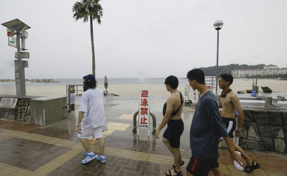 People walk past a swimming beach in Shirahama, Wakayama prefecture, western Japan Monday, Aug. 14, 2023. Swimming at the beach is banned due to approaching Typhoon Lan. The powerful typhoon was approaching Japan's main archipelago of Honshu on Monday threatening to hit large areas of western and central Japan with heavy rain and high winds, as many people were traveling for a Buddhist holiday week. A notice reads " No swimming." (Kyodo News via AP)