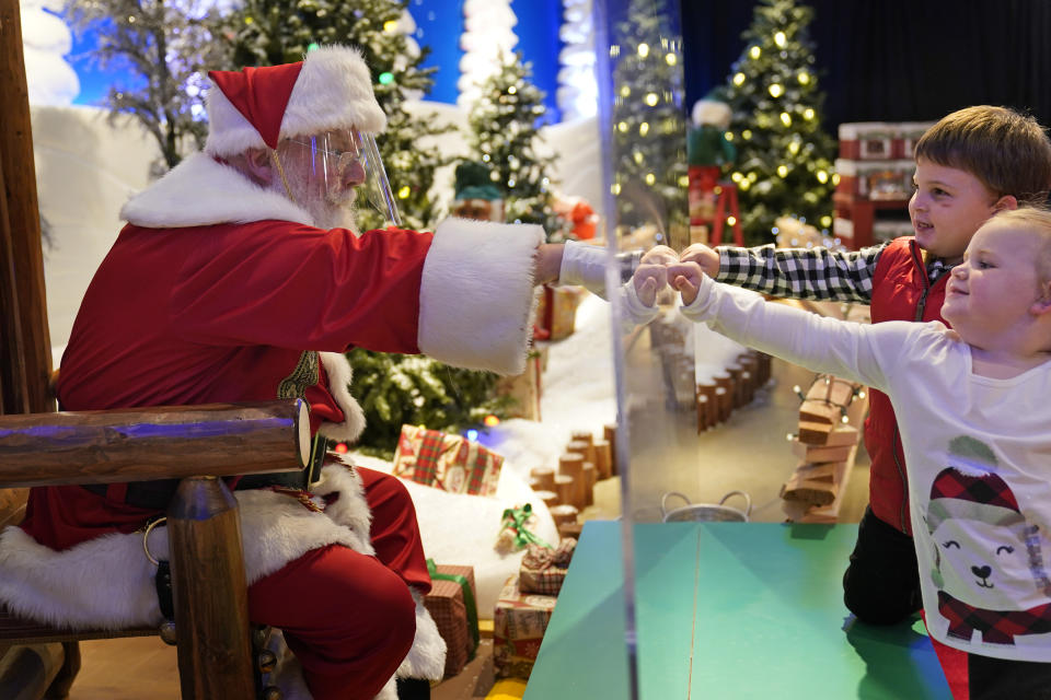 Julianna, 3, and Dylan Lasczak, 5, visit with Santa through a transparent barrier at a Bass Pro Shop in Bridgeport, Conn., on Nov. 10, 2020. In this socially distant holiday season, Santa Claus is still coming to towns (and shopping malls) across America but with a few 2020 rules in effect. (AP Photo/Seth Wenig)