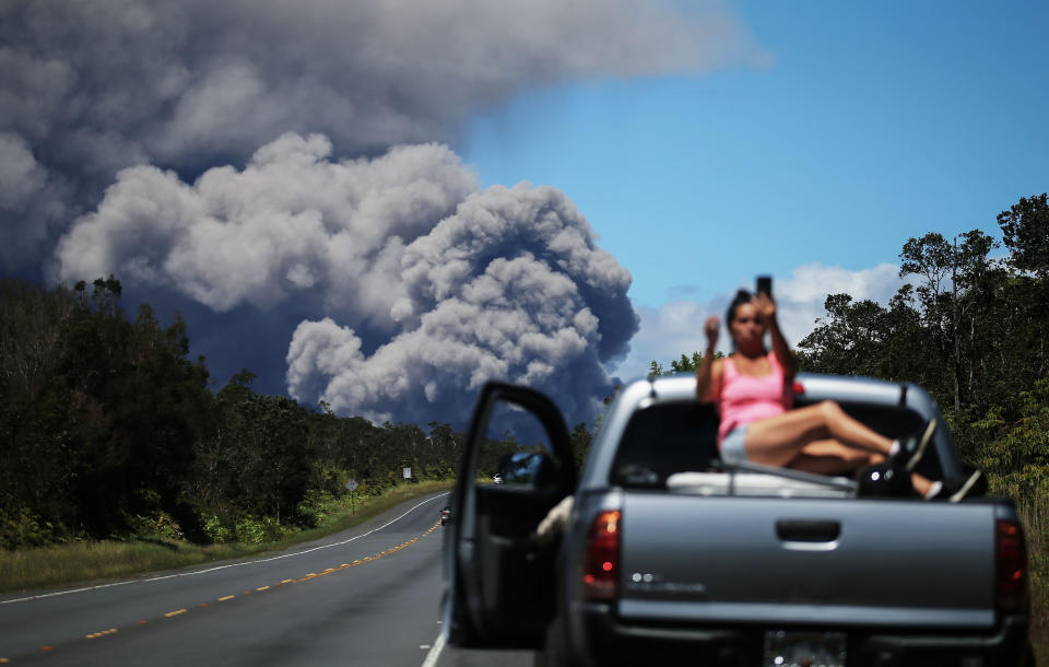 A woman takes a photo as an ash plume rises from the Kilauea volcano on Hawaii's Big Island on May 15, 2018.