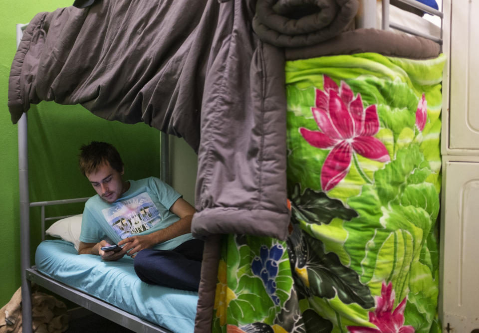 Sam Ware, 22, plays on his phone before going to bed at a hostel in The Entrance, Central Coast, Australia, Thursday, July 25, 2019. Sam's mother will no longer allow him to live at home. He's lost friends and family and most of his belongings through his addiction. His phones, laptop and clothes were left behind or stolen while overdosing on trains, in shopping centers, in a library. (AP Photo/David Goldman)