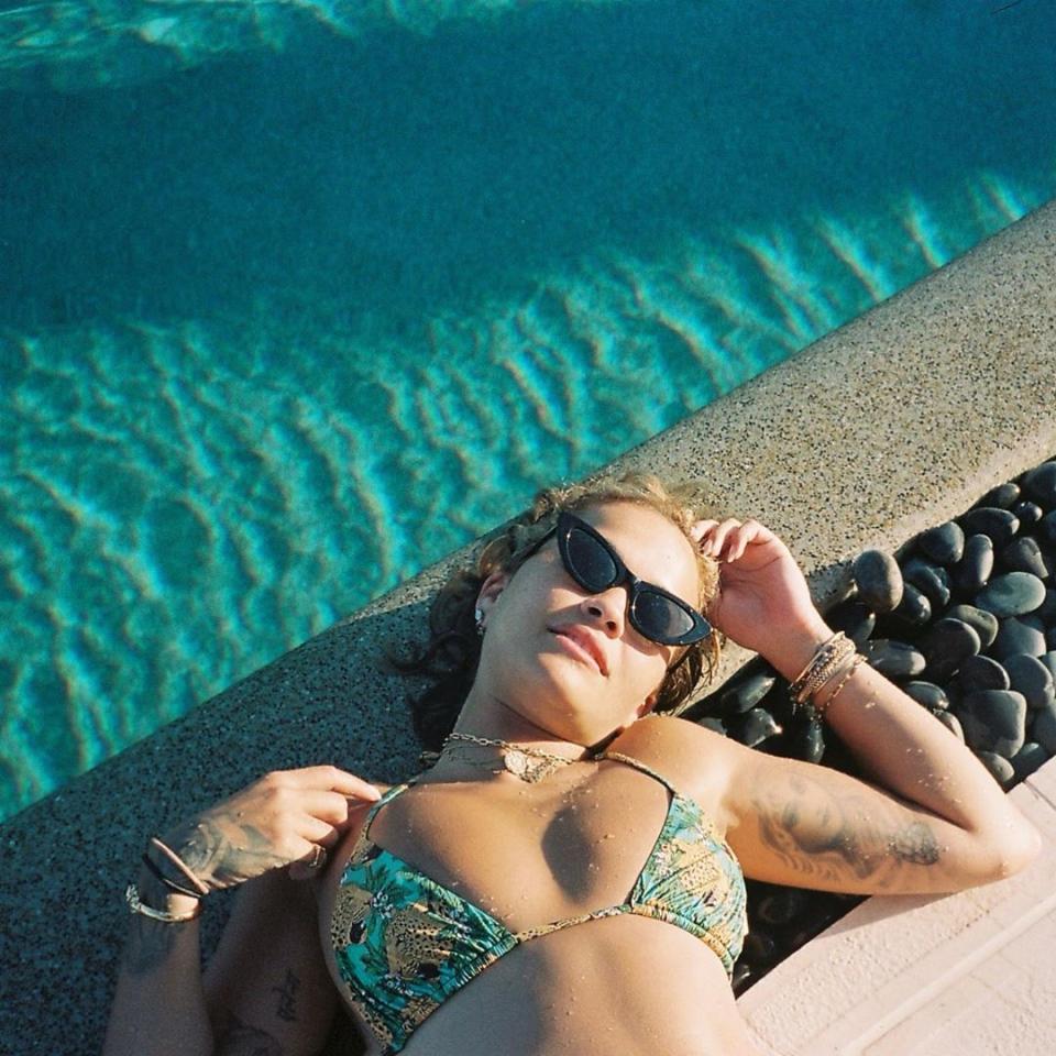 Rita Ora wearing a string bikini while lying next to a swimming pool