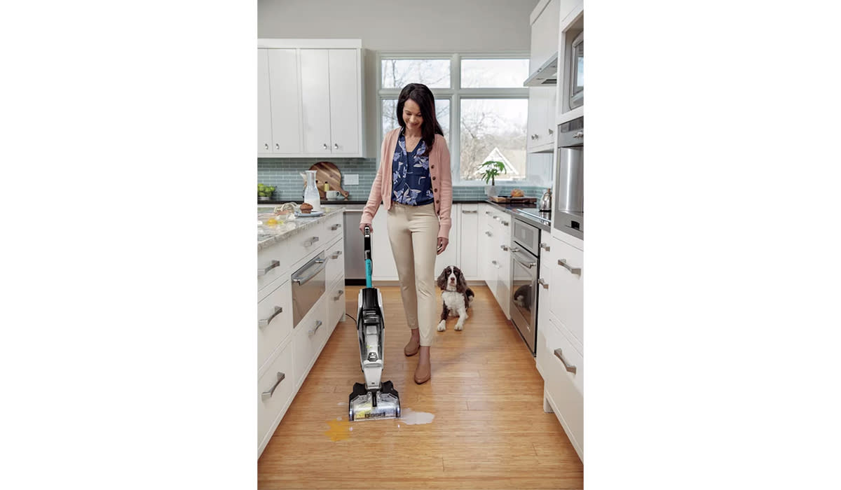 Woman using Bissel PetPro machine on a wet spill in the kitchen. You see her dog behind her.