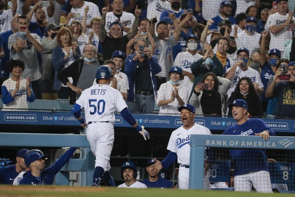 Dodgers manager Dave Roberts cheers and holds out his hand for Mookie Betts, who enters the dugout after a hitting a home run