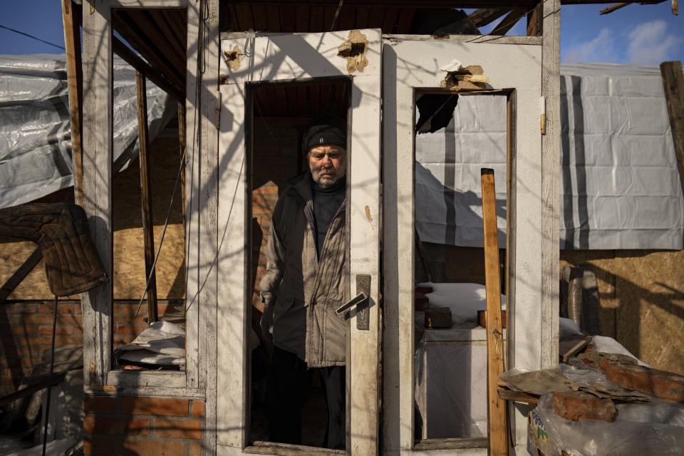 Oleksandr Luzhan, whose mother's house was struck twice, exits the shrapnel riddled building, in Kupiansk, Ukraine, Monday, Feb. 20, 2023. Luzhan picked up insulation kits, containing wooden boards and other items, supplied by an aid group called HEKS/EPER Swiss Church Aid and said to increase indoor temperatures in battered homes by at least 5 degrees to seal his mother's house. (AP Photo/Vadim Ghirda)