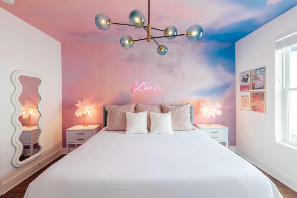 A bedroom with sky-painted walls and a neon sign that says "lover."