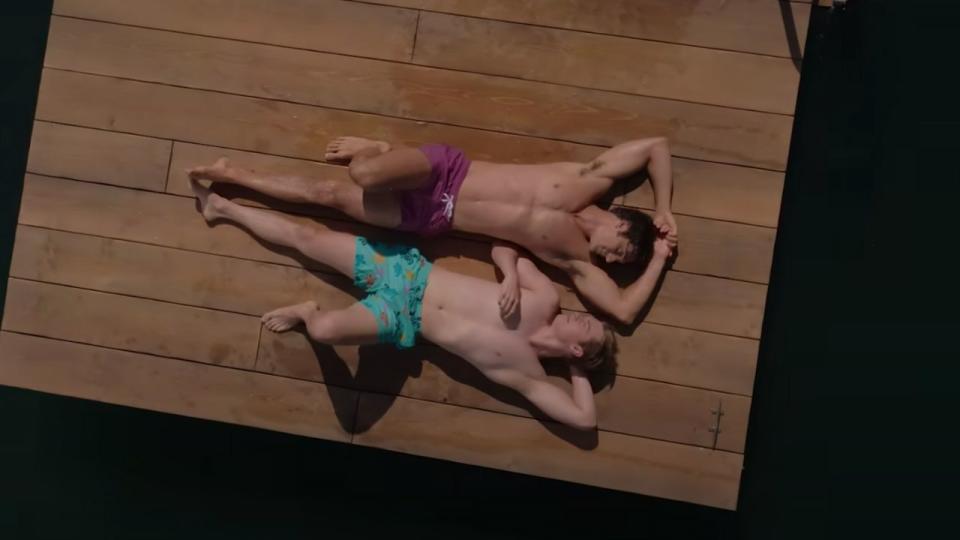 Alex and Henry lying in their swimming trunks on a floating dock