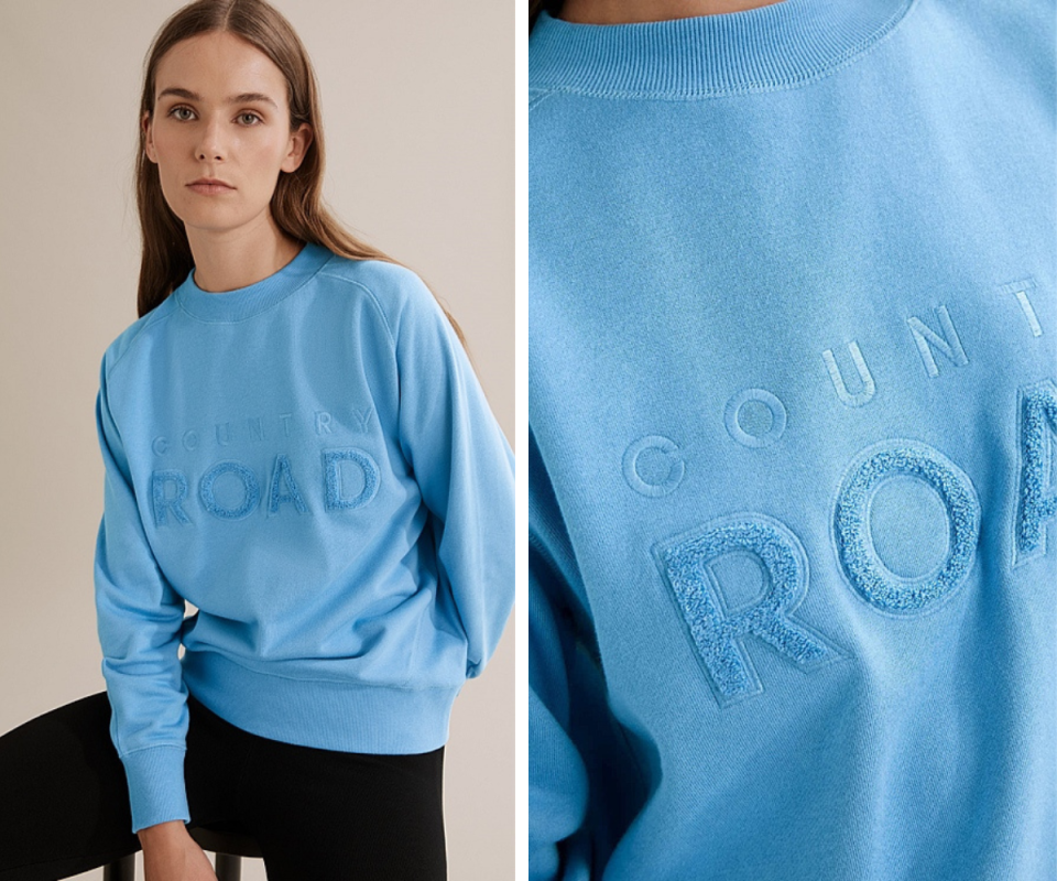 A brunette girl on the left wears a blue Country Road sweater with the logo embroidered in flocking, with a close-up of the logo on the right.