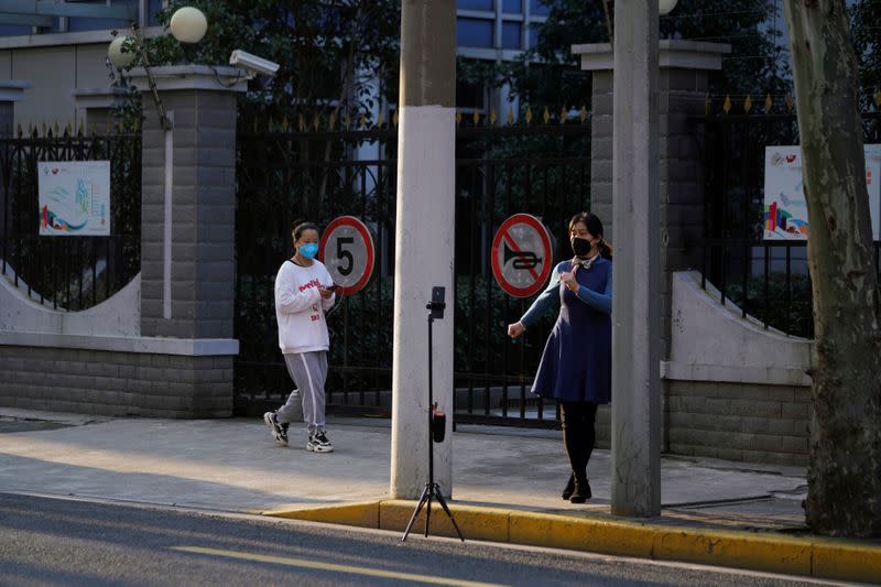A woman wearing a mask performs a dance to her friend via mobile phone on a street in downtown Shanghai