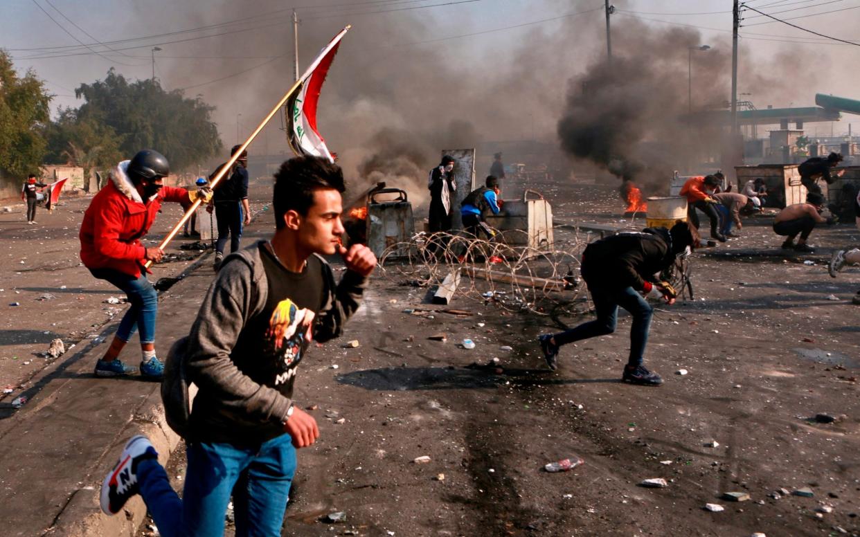 Anti-government protesters take cover while security forces use tear gas during clashes in central Baghdad, - AP
