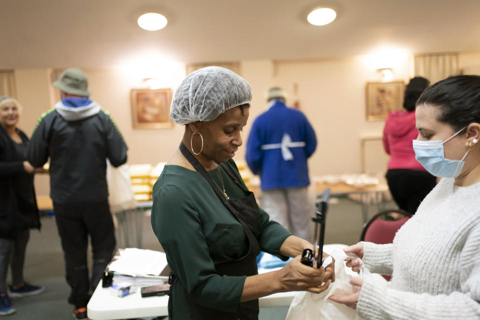 Chief coordinator Glenda Andrew speaks to a volunteer as she staples the address onto a bag set for delivery, at the Xaverian Sanctuary, in Preston, England, Friday Feb. 19, 2021. Once a week they distribute meals to people in Preston and surrounding communities in northwestern England that have recorded some of the U.K.’s highest coronavirus infection rates. The meal program grew out of Andrew’s work with Preston Windrush Generation & Descendants, a group organized to fight for the rights of early immigrants from the Caribbean and other former British colonies who found themselves threatened with deportation in recent years. (AP Photo/Jon Super)