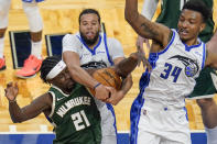 Milwaukee Bucks guard Jrue Holiday (21) goes after a rebound against Orlando Magic guard Michael Carter-Williams, center, and center Wendell Carter Jr. (34) during the second half of an NBA basketball game, Sunday, April 11, 2021, in Orlando, Fla. (AP Photo/John Raoux)