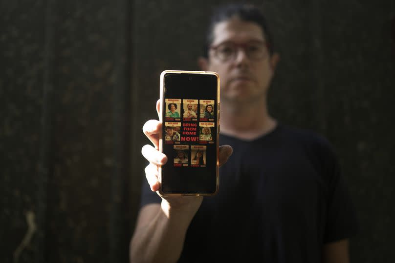 Yuval Haran, whose family is celebrating the return of his mother, his sister, and four others from Hamas captivity, displays a picture of his family's hostage posters