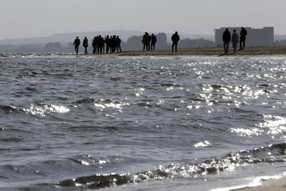 People stand at the beach and watch the Famagusta or Varosia abandoned city before the epiphany ceremony to bless the sea in the Turkish occupied area at north part of the eastern Mediterranean divided island of Cyprus, Monday, Jan. 6, 2020. Many Orthodox Christian faithful attended the Epiphany Day blessing of the waters in Famagusta in Cyprus', the fifth time the ceremony has taken place since 1974 when the small island nation was cleaved along ethnic lines. (AP Photo/Petros Karadjias)