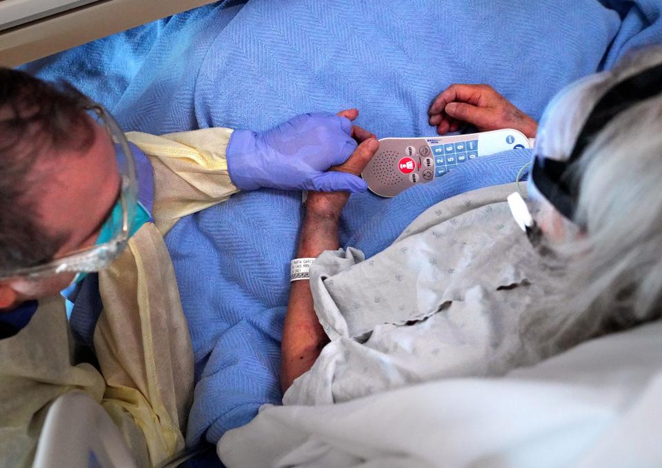 Chaplain Kevin Deegan holds a patient's hand while praying with her on Friday, Feb. 12, 2021, on the COVID floor at Providence Holy Cross Medical Center in Los Angeles. "I'll never be afraid of donning PPE to go and sit and hold the patient's hand, to brush their hair with my hand, to lay my hands on them and pray with them," Deegan said. "Fear is not a part of the care that I'm offering anymore."