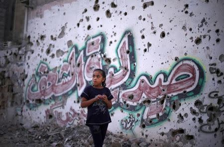 A Palestinian girl walks past a pharmacy's wall, which witnesses said was damaged during the Israeli offensive, in the east of Gaza City September 10, 2014. REUTERS/Suhaib Salem/Files