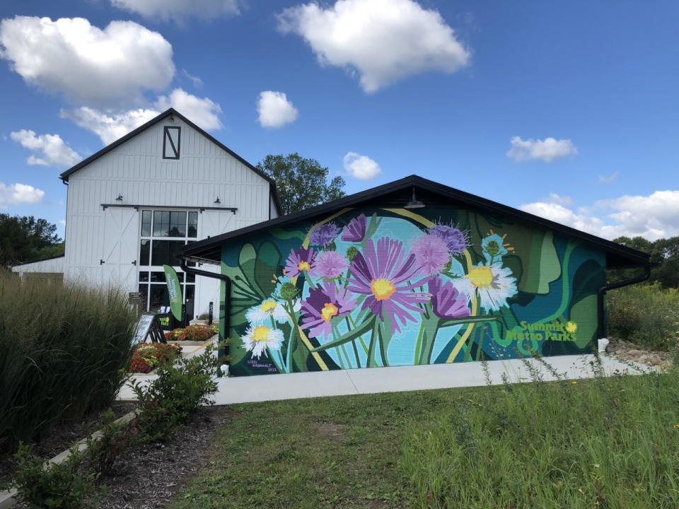 A mural by Akron artist Lizzi Aronhalt is painted on a building, with the Himelright Lodge in the background, in the Valley View Area of Cascade Valley Metro Park in Akron.