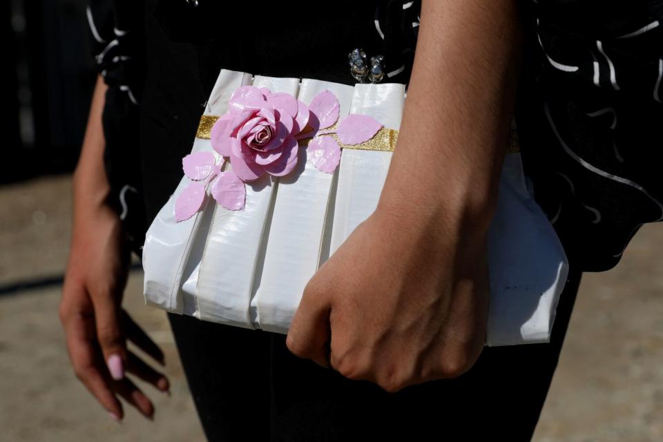 A hand holds a white duct tape handbag decorated with a pink flower