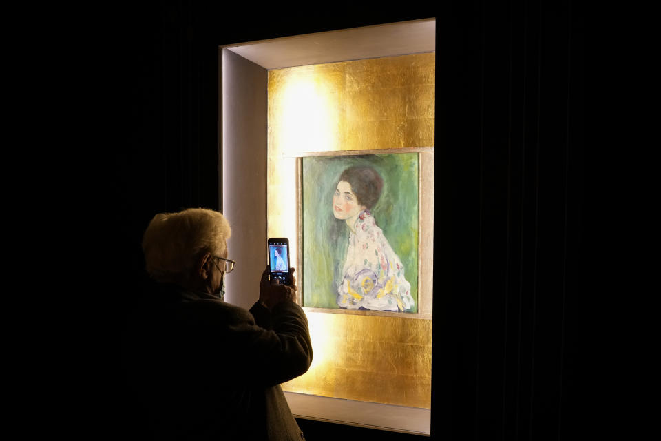 A woman takes a photo of Gustav Klimt's oil on canvas painting "Portrait of a Lady" (1916/17) on display at the exhibition "Klimt. The Secession and Italy" at the Museum of Rome, in Palazzo Braschi, Rome, during a press preview, Tuesday, Oct. 26, 2021. The exhibition, that explores Klimt's period in Italy, will be open to visitors from Oct.27, 2021 to March 27, 2022. (AP Photo/Andrew Medichini)