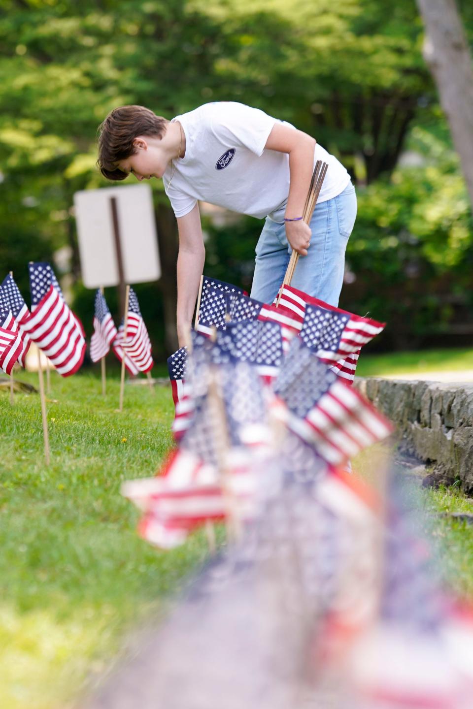 Cliffside Park High School freshman Tyler Jerred places American flags along the front lawn of the high school with other student volunteers to honor those who died in combat ahead of Memorial Day on Monday, May 22, 2023.