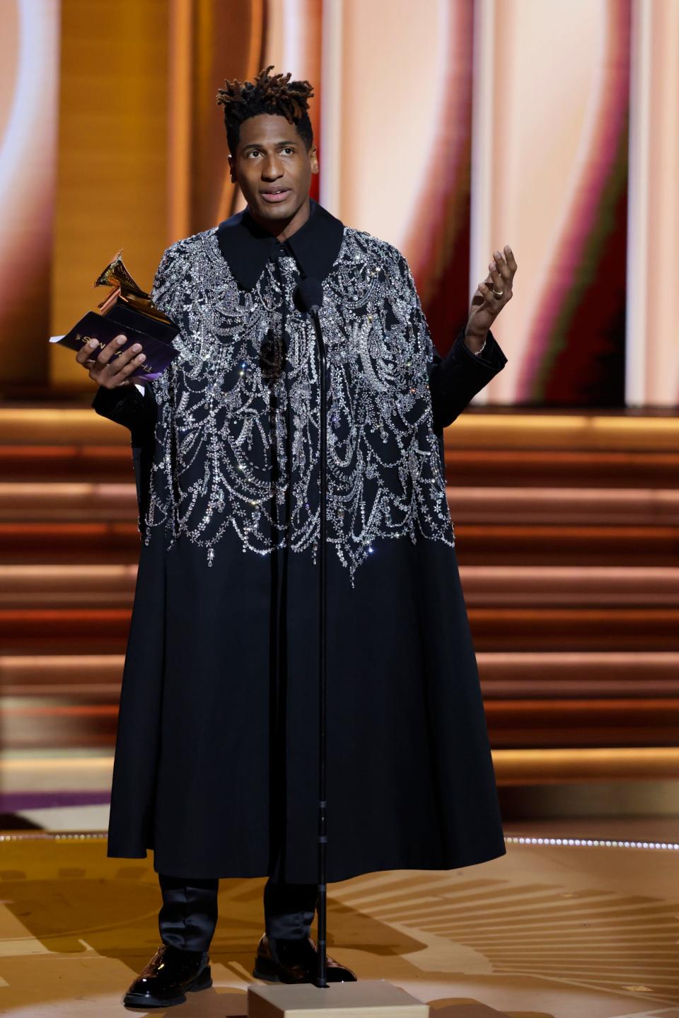 Jon in a black ankle-length cape coat with silver sparkling embellishments from the collar down to mid-coat.