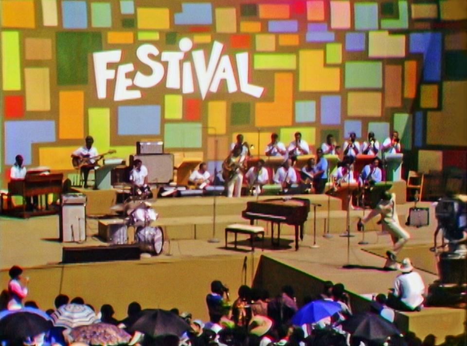 A stage at the Harlem Culture Festival in 1969. The stage is colorful with a backdrop of colorful squares with the word "Festival." A band performs.