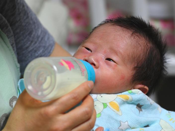 An image of a South Korean baby being bottle-fed milk by a social worker.