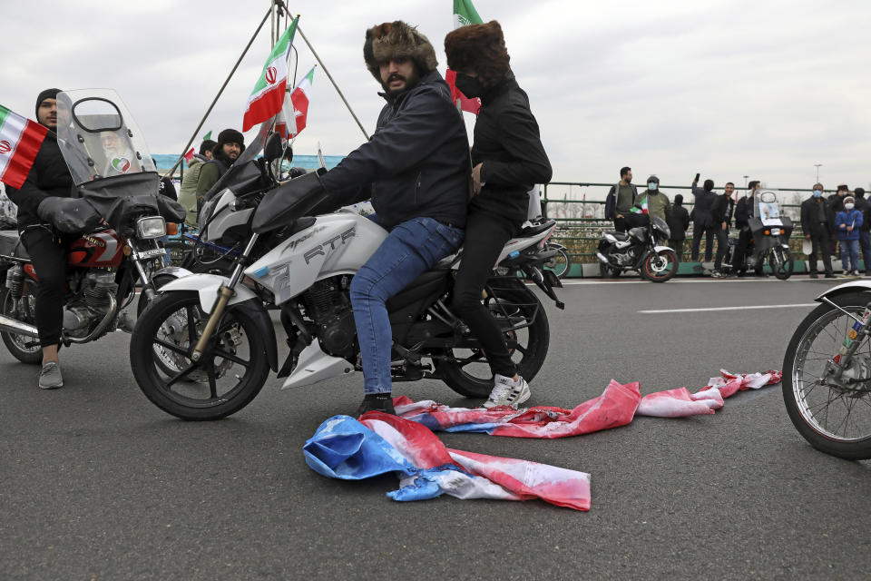 A man on a motorcycle pulls a burnt representation of the U.S. flag on the ground during the annual rally commemorating the anniversary of1979 Islamic Revolution in Tehran, Iran, Friday, Feb. 11, 2022. Thousands of cars and motorbikes paraded in the celebration, although fewer pedestrians were out for a second straight year due to concerns over the coronavirus pandemic. (AP Photo/Vahid Salemi)