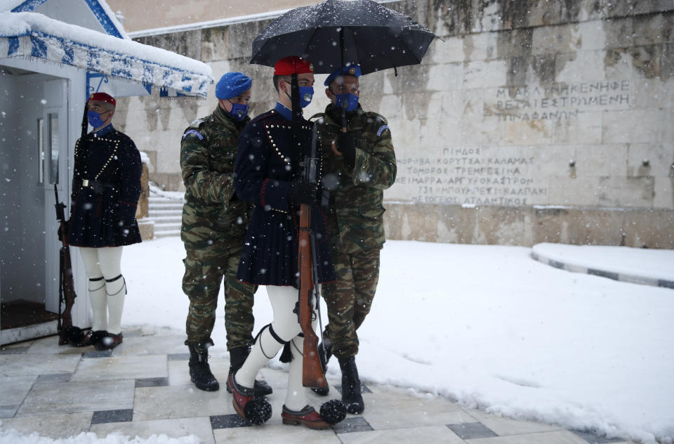 Soldiers help a member of the Presidential Guard, known as Evzonas, during the changing of the guard as snow falls at the tomb of the Unknown Soldier in Athens, Tuesday, Feb.16, 2021. A cold weather front has hit Greece, sending temperatures plunging from the low 20s Celsius (around 70 Fahrenheit) on Friday to well below freezing on Tuesday, and heavy snowfall in central Athens. (AP Photo/Thanassis Stavrakis)