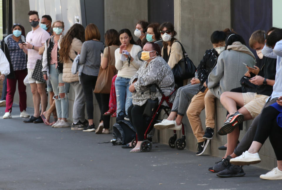 Dozens of people in masks line up in Melbourne to get a coronavirus test.