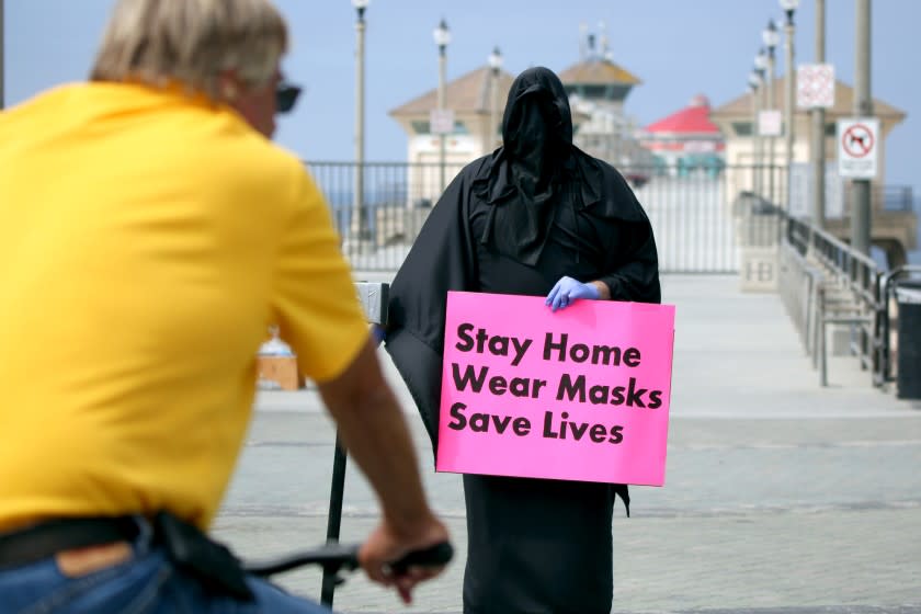 The Grim Reaper, also known as Spencer Kelly, holds a sign at Pier Plaza in Huntington Beach on Friday. The Huntington Beach resident was part of a three-person protest organized by Indivisible OC 48.(Raul Roa / Times Community News)