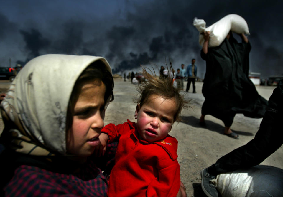 An Iraqi girl holds her sister as she waits for her mother (R) to bring over food bought in Basra March 29, 2003. Iraqi forces still hold the centre of Iraq's second city Basra and British troops fighting for control of the country's southeast do not plan to rush in, a British army spokesman said on Saturday. REUTERS/Jerry Lampen