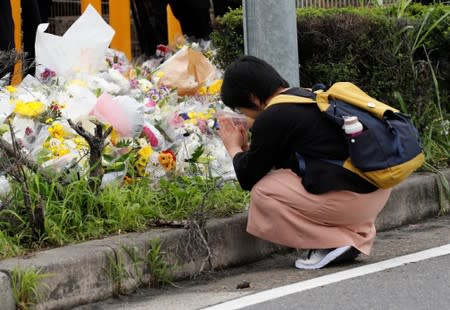 A woman prays in front of a row of flowers placed for victims of the torched Kyoto Animation building in Kyoto