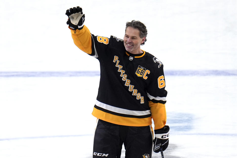 Former Pittsburgh Penguins player Jaromir Jagr stands at center ice and waves to fans after skating during warm ups after having a banner with his retired uniform number raised to the rafters of PPG Paints arena before an NHL hockey game between the Los Angeles Kings and Pittsburgh Penguins in Pittsburgh, Sunday, Feb. 18, 2024. (AP Photo/Gene Puskar)