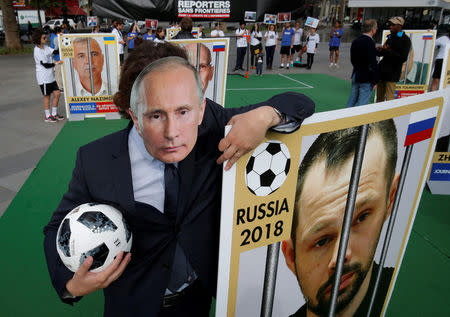 A Reporter Without Borders (RSF) activist, wearing a mask depicting Russian President Vladimir Putin, stands next to a giant portrait of journalist Alexei Kungurov on Place de la Republique, transformed into a soccer field to denounce abuse of press freedom in Russia before the start of the 2018 FIFA World Cup Russia, in Paris, France, June 13, 2018. REUTERS/Philippe Wojazer