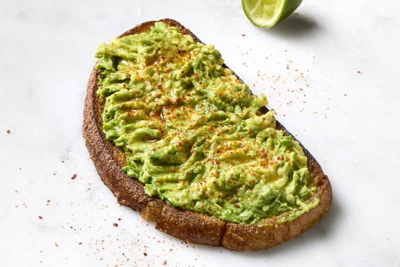 avocado toast on a marble background, sprinkled with Tajin and with a lime wedge squeezed next to it.