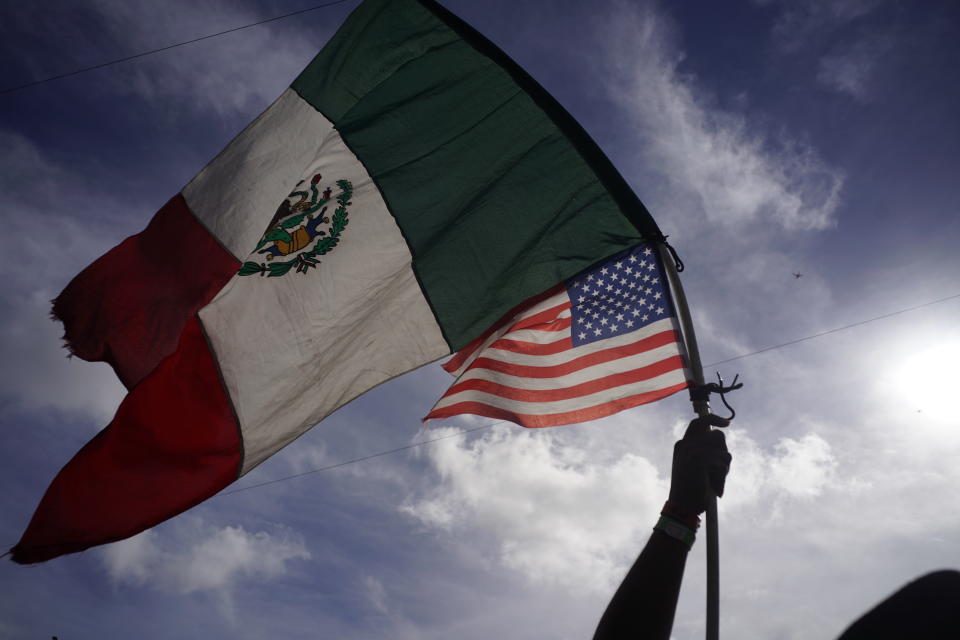 A Honduran migrant holds up Mexican and U.S. flags as he joins a small group of migrants trying to cross the border together at the Chaparral border crossing in Tijuana, Mexico, Thursday, Nov. 22, 2018. A small group of Central American migrants marched peacefully to the border crossing in Tijuana Thursday to demand better conditions and push to enter the U.S. (AP Photo/Ramon Espinosa)