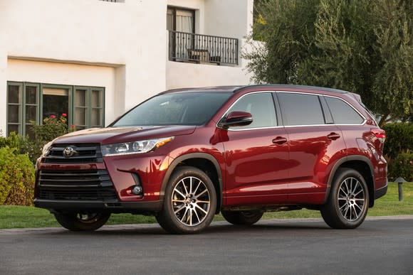 A red Toyota Highlander, a midsize crossover SUV, in front of a home.