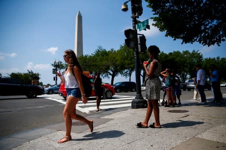 People walk along Constitution Avenue near the Washington Monument during a heat wave in Washington