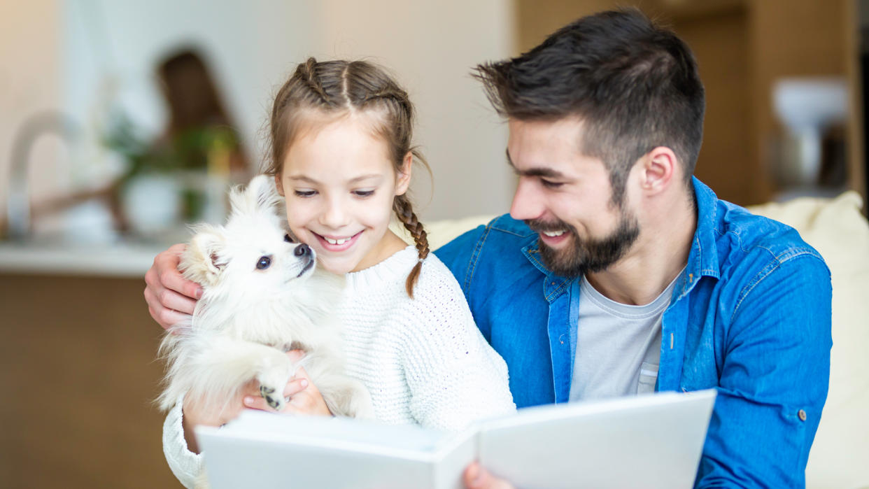  Father and daughter reading a book, daughter holding Pomeranian. 