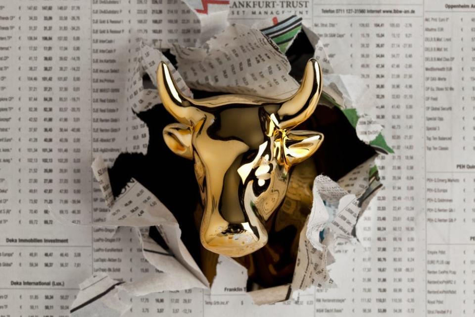 Gold bull emerging through newspaper