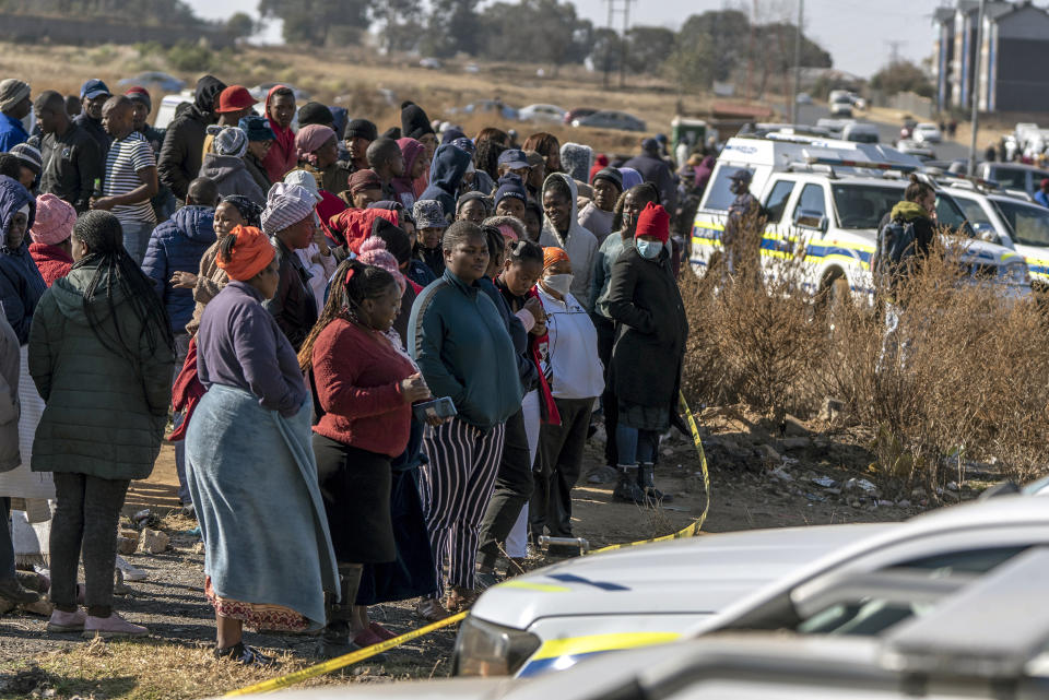 People look on at the scene of an overnight bar shooting in Soweto, South Africa, Sunday July 10, 2022. A mass shooting at a tavern in Johannesburg's Soweto township has killed 15 people and left others in critical condition, according to police. Police say they are investigating reports that a group of men arrived in a minibus taxi and opened fire on some of the patrons at the bar shortly after midnight Sunday. (AP Photo/Shiraaz Mohamed)